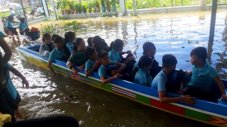 Students in blue uniforms packed into a colorful long boat that serves as their school transport during flood season