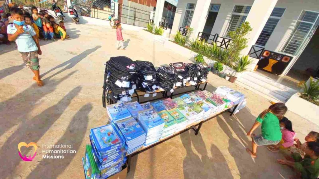 A table outside the new school covered with stacks of colorful Khmer-language textbooks and rows of new black backpacks, ready for the students to receive